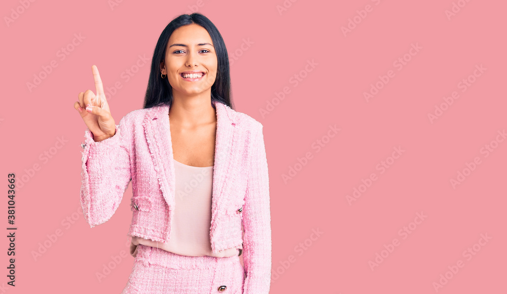 Young beautiful latin girl wearing business clothes showing and pointing up with finger number one while smiling confident and happy.