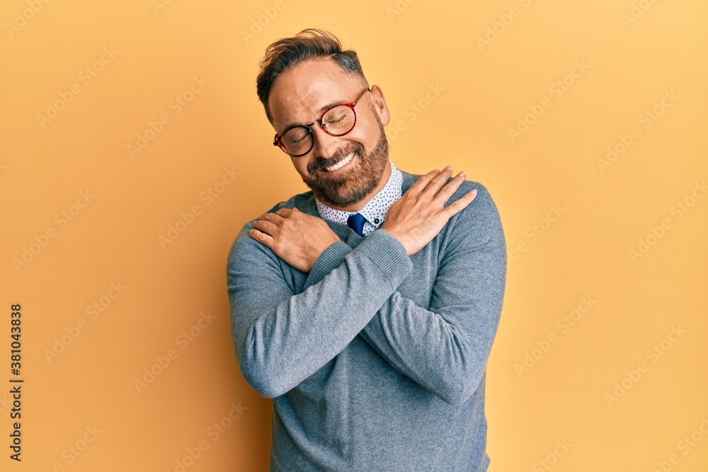 Handsome middle age man wearing glasses hugging oneself happy and positive, smiling confident. self love and self care Handsome middle age man wearing glasses hugging oneself happy and positive, smiling confident. self love and self care