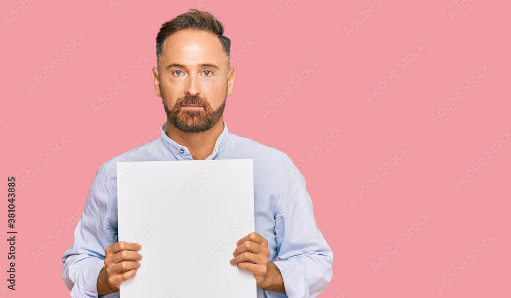 Handsome middle age man holding blank empty banner thinking attitude and sober expression looking self confident Handsome middle age man holding blank empty banner thinking attitude and sober expression looking self confident