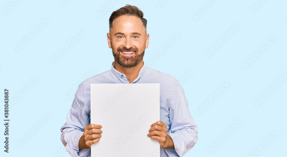 Handsome middle age man holding blank empty banner looking positive and happy standing and smiling with a confident smile showing teeth Handsome middle age man holding blank empty banner looking positive and happy standing and smiling with a confident smile showing teeth