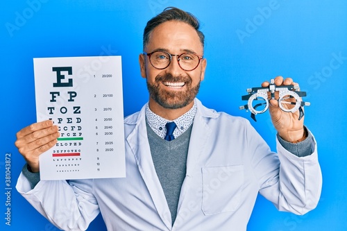 Handsome middle age man holding optometry glasses and medical exam smiling with a happy and cool smile on face. showing teeth. photo