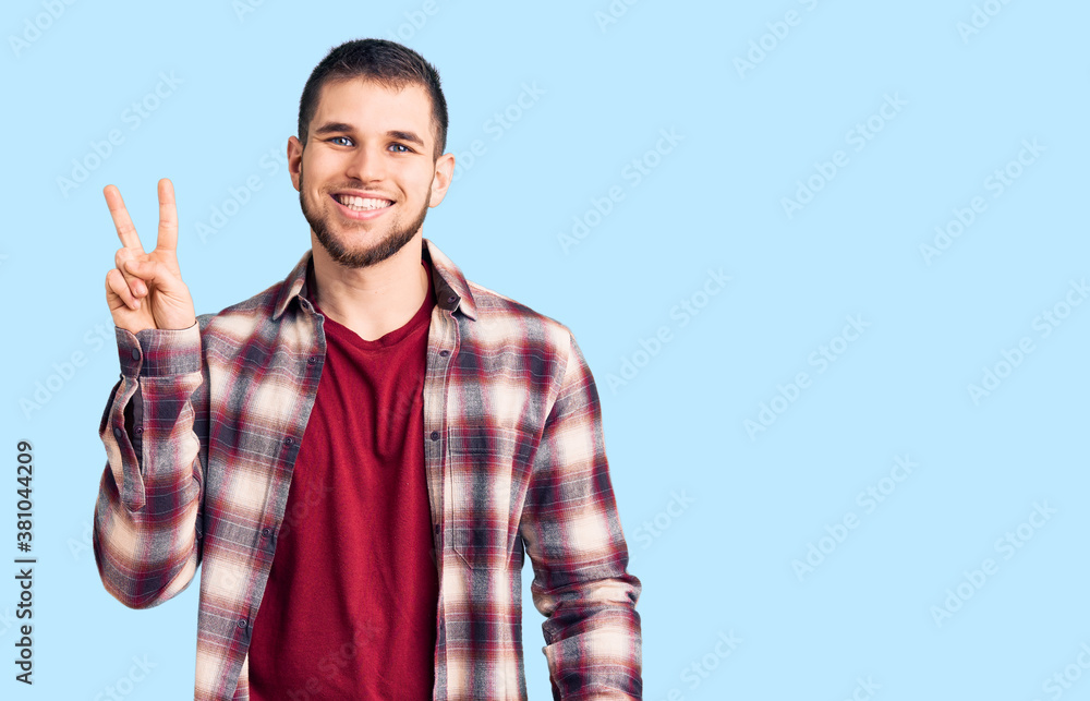 Young handsome man wearing casual shirt smiling looking to the camera showing fingers doing victory sign. number two. Young handsome man wearing casual shirt smiling looking to the camera showing fingers doing victory sign. number two.