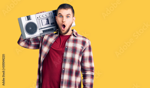 Young handsome man listening to music holding boombox scared and amazed with open mouth for surprise, disbelief face