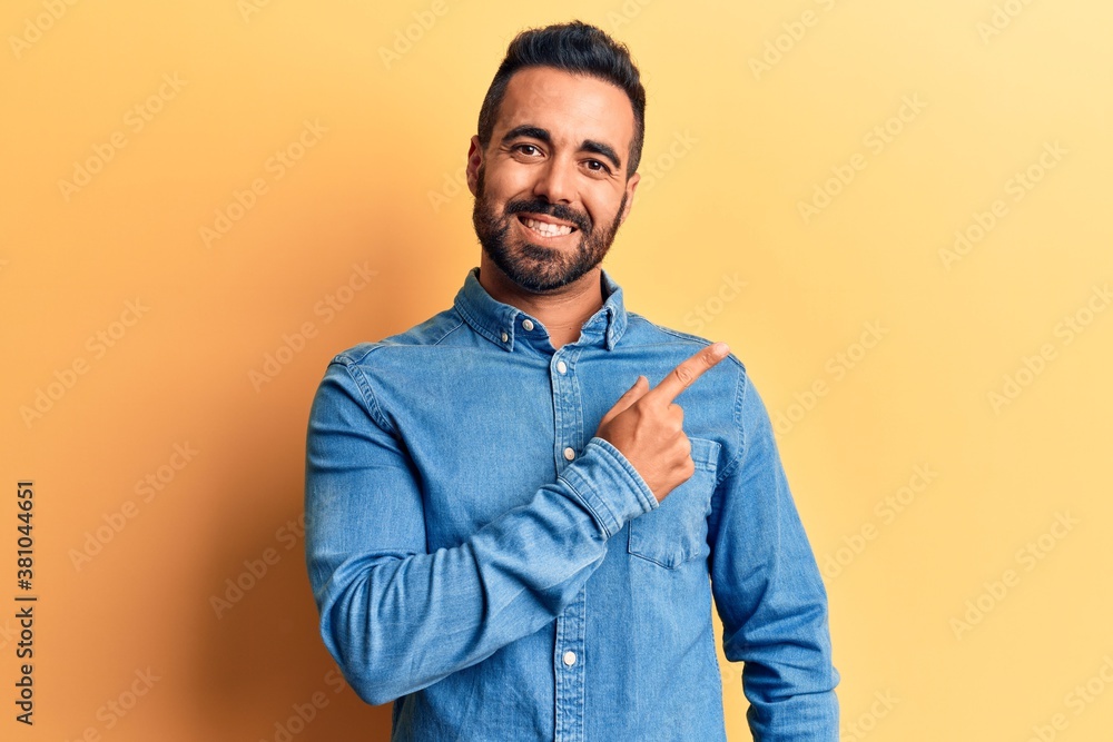 Young hispanic man wearing casual clothes cheerful with a smile of face pointing with hand and finger up to the side with happy and natural expression on face Young hispanic man wearing casual clothes cheerful with a smile of face pointing with hand and finger up to the side with happy and natural expression on face