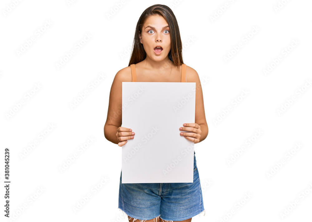 Young caucasian woman holding blank empty banner scared and amazed with open mouth for surprise, disbelief face Young caucasian woman holding blank empty banner scared and amazed with open mouth for surprise, disbelief face