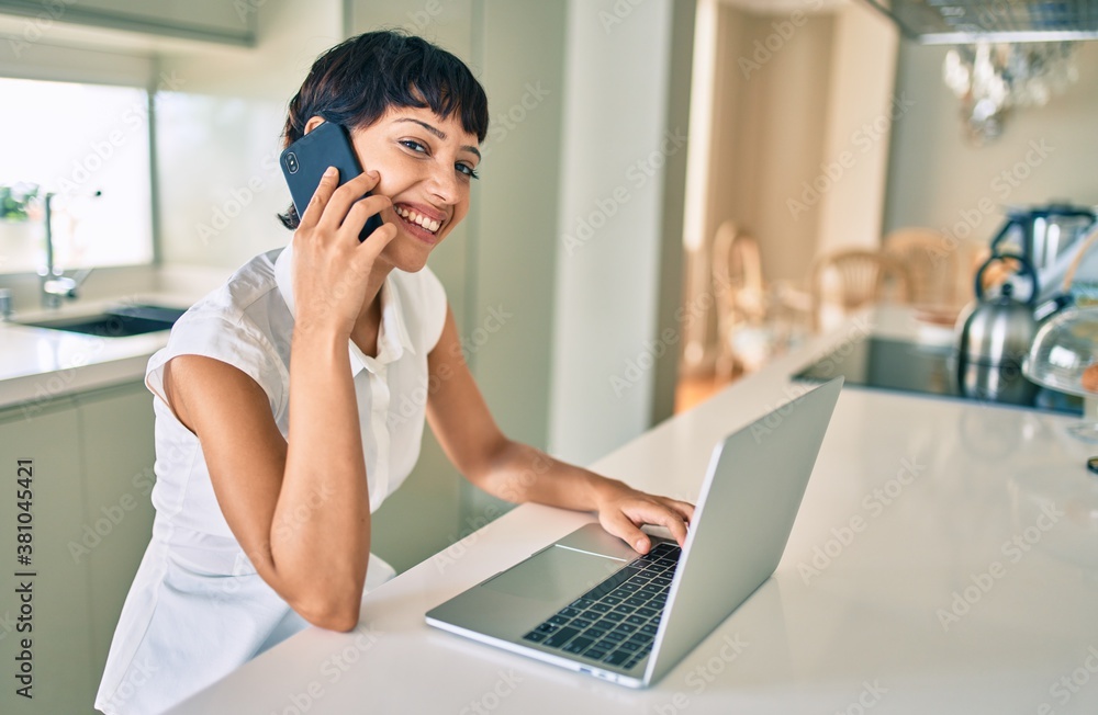 Beautiful brunette woman with short hair at home using computer laptop speaking on the phone Beautiful brunette woman with short hair at home using computer laptop speaking on the phone