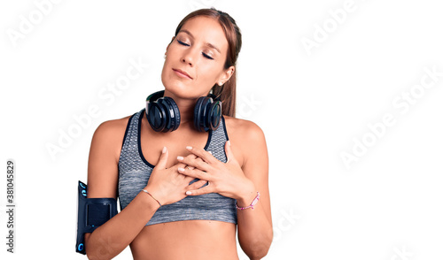 Young beautiful hispanic woman wearing gym clothes and using headphones smiling with hands on chest with closed eyes and grateful gesture on face. health concept.