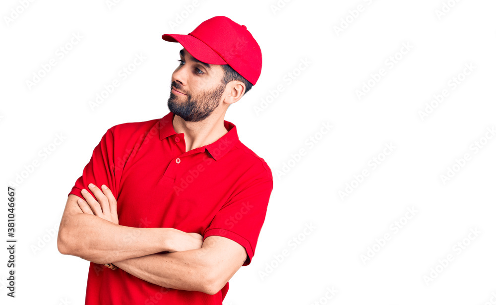 Young handsome man with beard wearing delivery uniform looking to the side with arms crossed convinced and confident