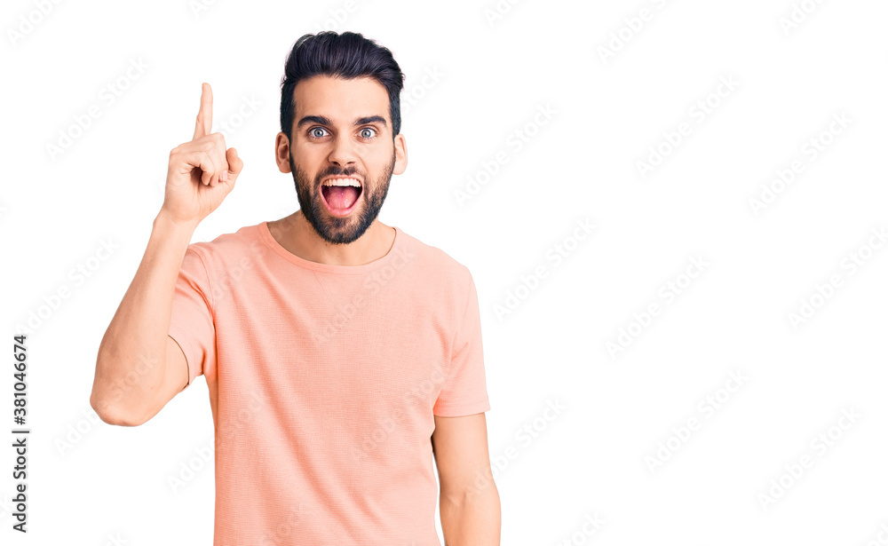 Young handsome man with beard wearing casual t-shirt pointing finger up with successful idea. exited and happy. number one. Young handsome man with beard wearing casual t-shirt pointing finger up with successful idea. exited and happy. number one.