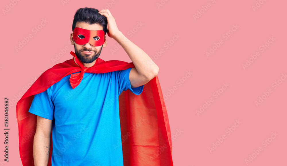 Young handsome man with beard wearing super hero costume confuse and wonder about question. uncertain with doubt, thinking with hand on head. pensive concept.