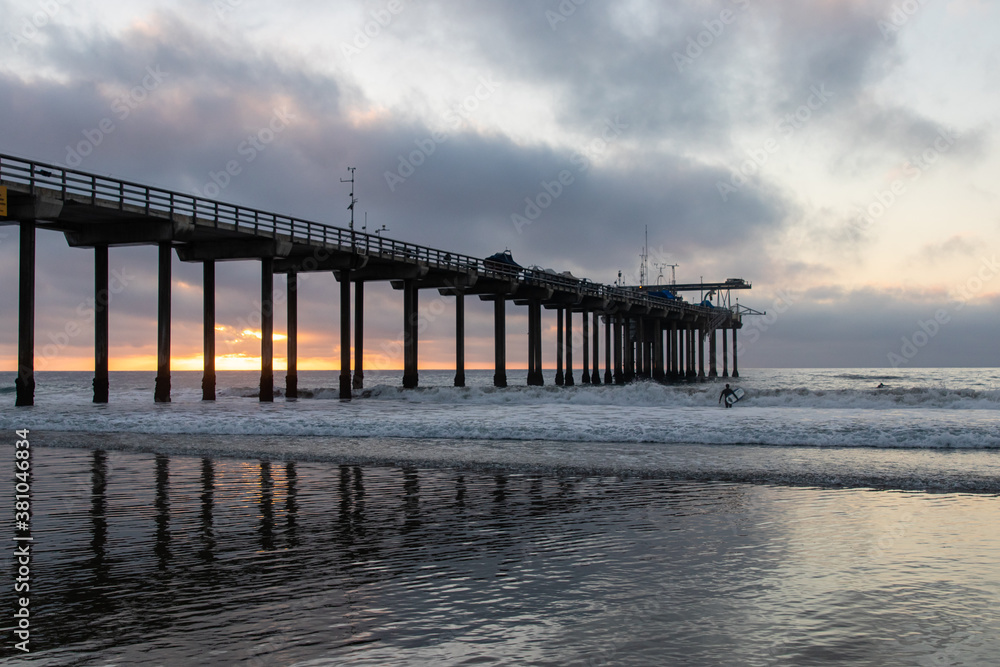Scripps Pier in San Diego California during sunset with moody clouds over waves and sand.