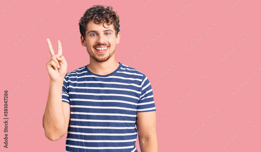 Young handsome man with curly hair wearing casual clothes showing and pointing up with fingers number two while smiling confident and happy. Young handsome man with curly hair wearing casual clothes showing and pointing up with fingers number two while smiling confident and happy.