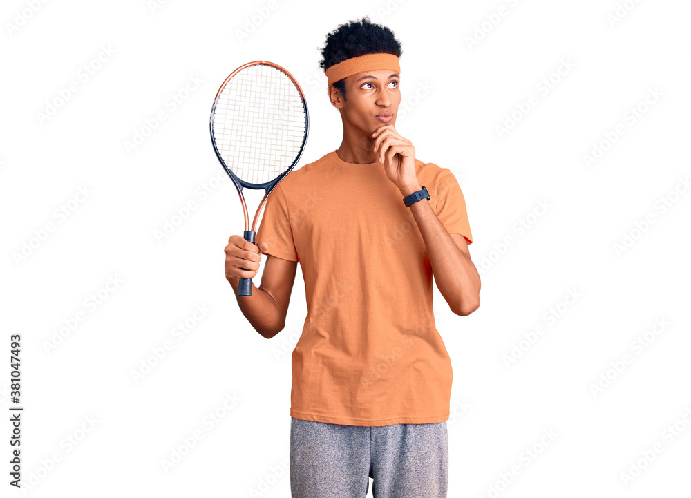 Young african american man playing tennis holding racket serious face thinking about question with hand on chin, thoughtful about confusing idea Young african american man playing tennis holding racket serious face thinking about question with hand on chin, thoughtful about confusing idea