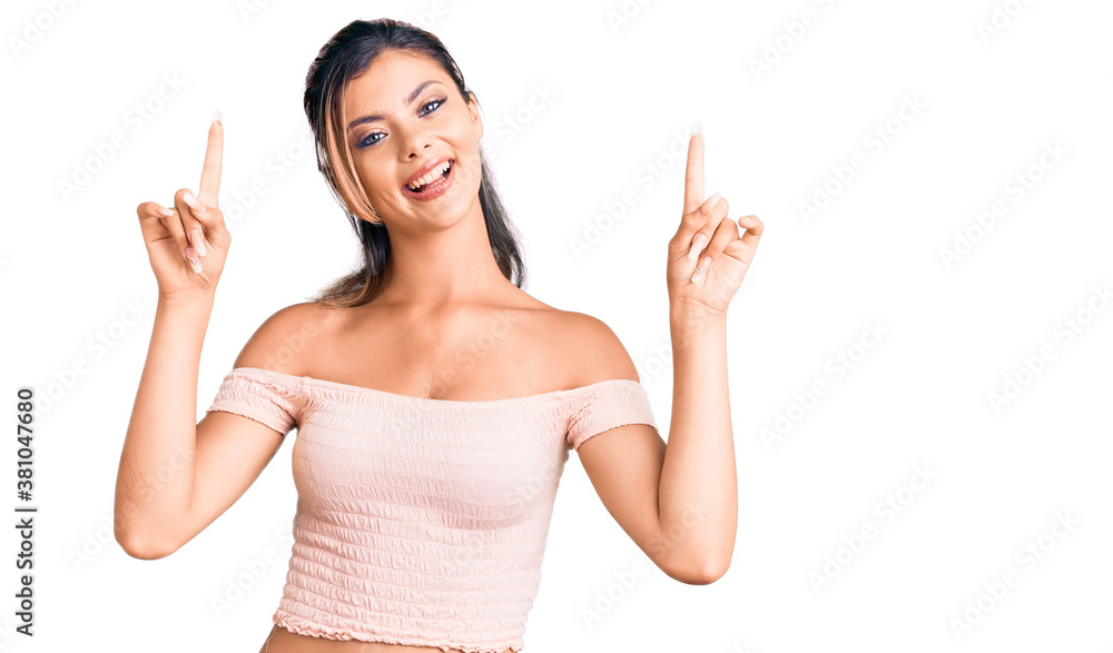 Young beautiful woman wearing casual clothes smiling amazed and surprised and pointing up with fingers and raised arms. Young beautiful woman wearing casual clothes smiling amazed and surprised and pointing up with fingers and raised arms.