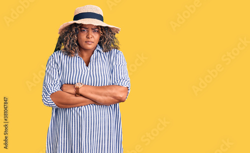 Young african american plus size woman wearing summer hat skeptic and nervous, disapproving expression on face with crossed arms. negative person.
