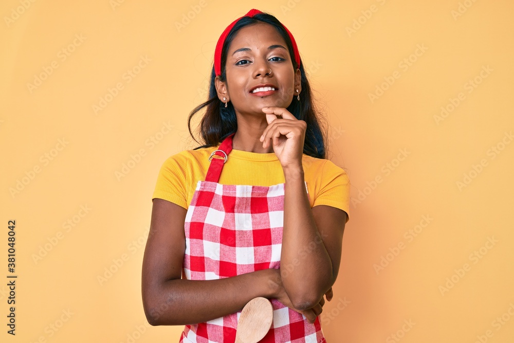 Young indian girl wearing baker apron smiling looking confident at the camera with crossed arms and hand on chin. thinking positive. Young indian girl wearing baker apron smiling looking confident at the camera with crossed arms and hand on chin. thinking positive.