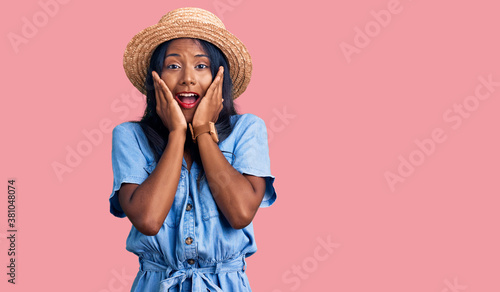 Young indian girl wearing summer hat afraid and shocked, surprise and amazed expression with hands on face
