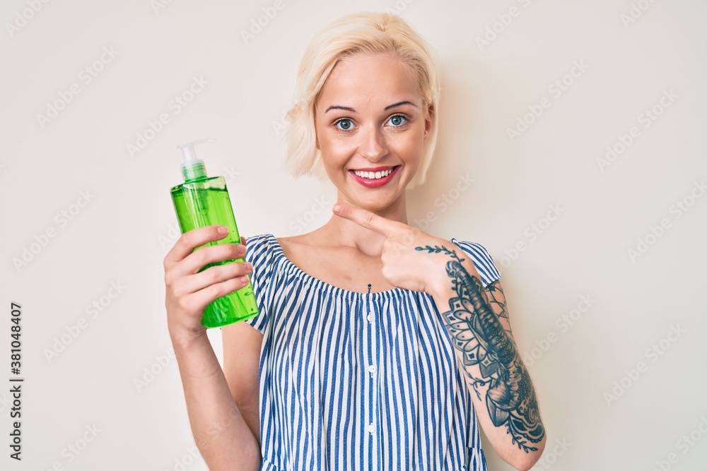 Young blonde woman with tattoo holding aloe vera smiling happy pointing with hand and finger Young blonde woman with tattoo holding aloe vera smiling happy pointing with hand and finger