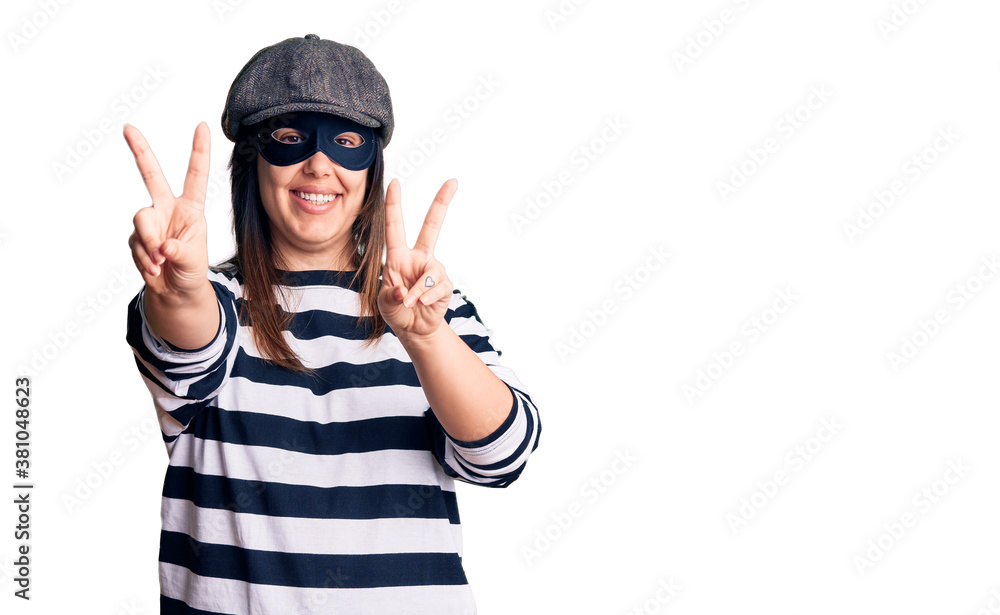 Young beautiful brunette woman wearing burglar mask smiling looking to the camera showing fingers doing victory sign. number two. Young beautiful brunette woman wearing burglar mask smiling looking to the camera showing fingers doing victory sign. number two.