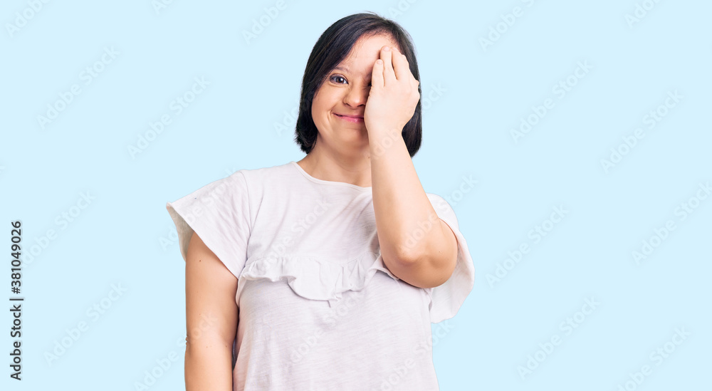 Brunette woman with down syndrome wearing casual white tshirt covering one eye with hand, confident smile on face and surprise emotion. Brunette woman with down syndrome wearing casual white tshirt covering one eye with hand, confident smile on face and surprise emotion.