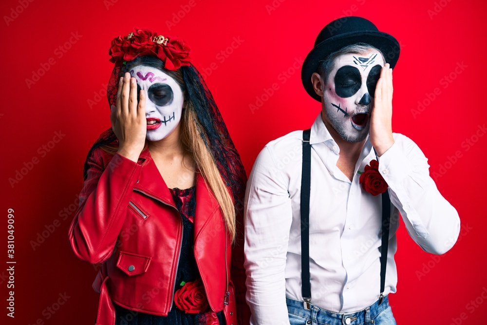 Couple wearing day of the dead costume over red yawning tired covering half face, eye and mouth with hand. face hurts in pain. Couple wearing day of the dead costume over red yawning tired covering half face, eye and mouth with hand. face hurts in pain.