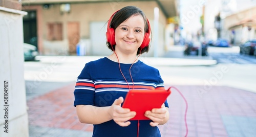 Beautiful brunette woman with down syndrome at the town on a sunny day using touchpad device listening to music wearing headphones