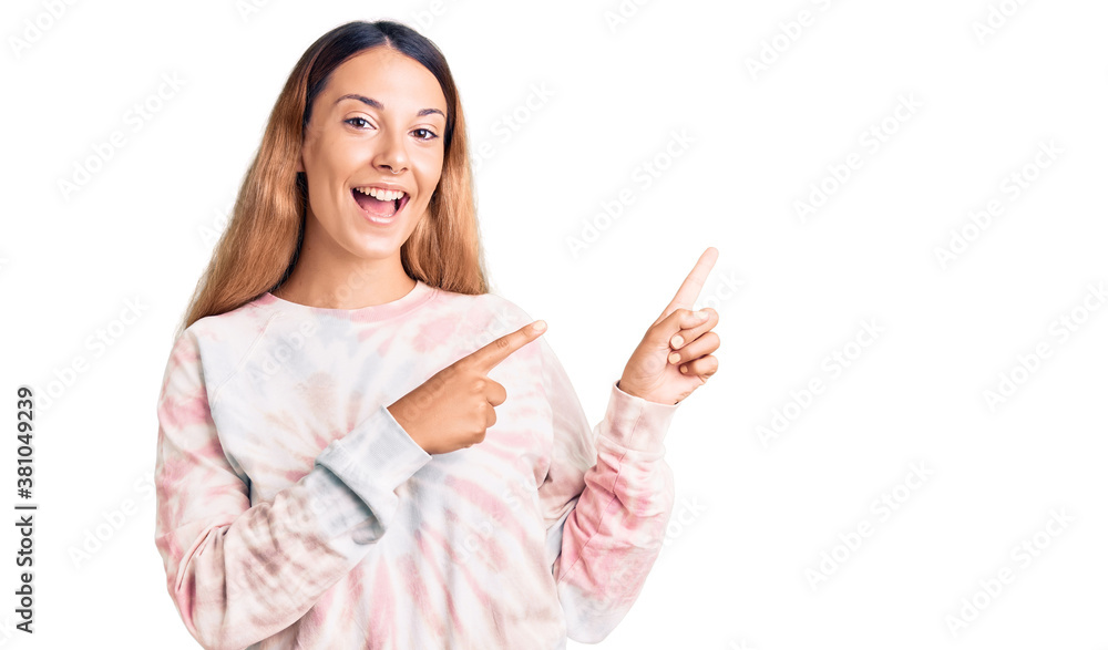 Beautiful young woman wearing casual tie dye sweatshirt smiling and looking at the camera pointing with two hands and fingers to the side. Beautiful young woman wearing casual tie dye sweatshirt smiling and looking at the camera pointing with two hands and fingers to the side.