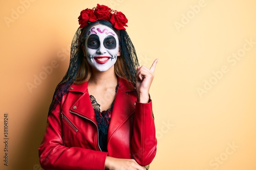Woman wearing day of the dead costume over yellow smiling happy pointing with hand and finger to the side © Krakenimages.com