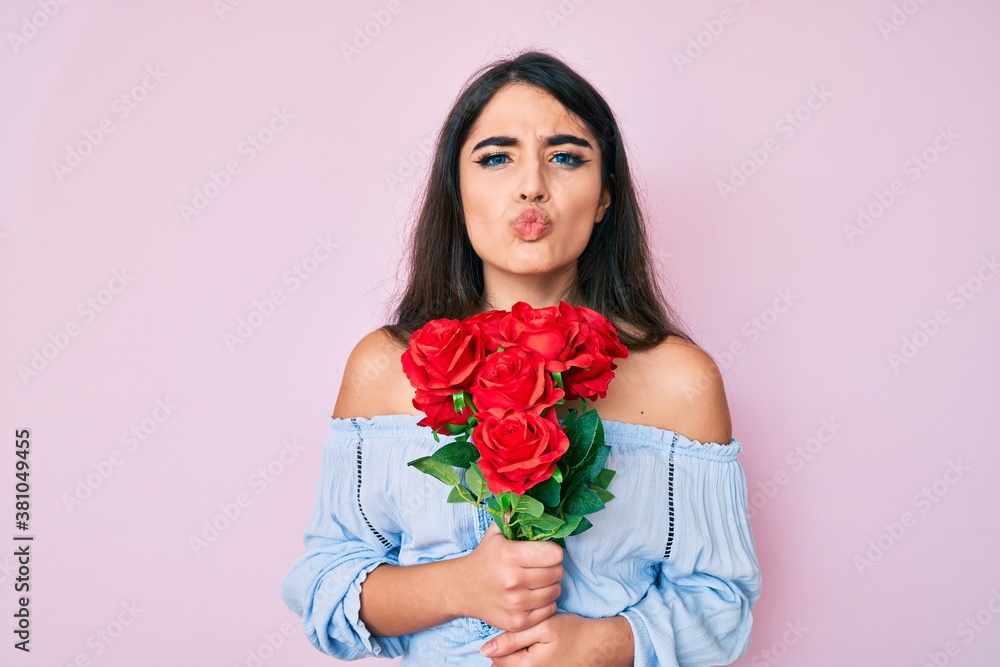 Brunette teenager girl holding flowers looking at the camera blowing a kiss being lovely and sexy. love expression. Brunette teenager girl holding flowers looking at the camera blowing a kiss being lovely and sexy. love expression.