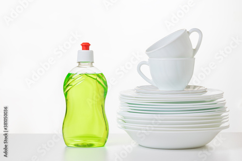 Fotografija Green dish washing gel and a set of plates on a light background.
