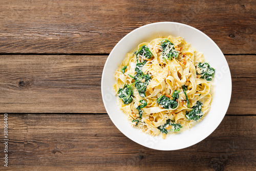 Foto Pasta fettuccine with spinach in creamy cheese sauce on a wooden background