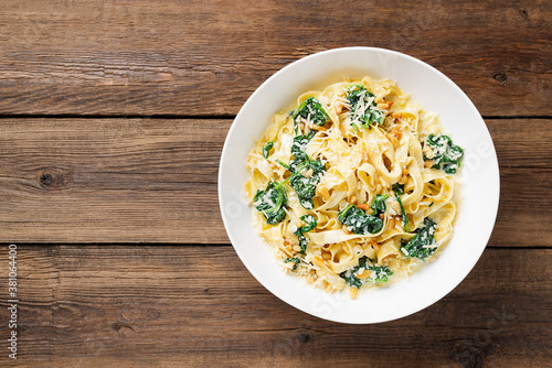 Pasta fettuccine with spinach in creamy cheese sauce on a wooden background.