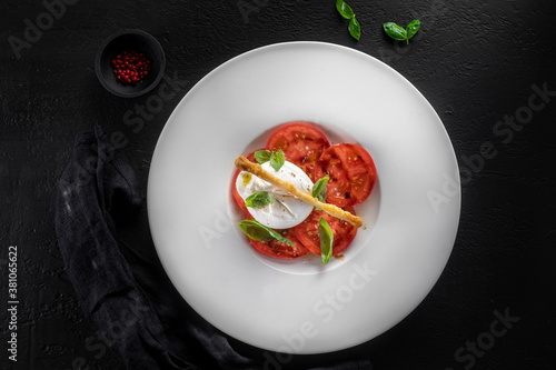 Burrata cheese and tomato salad with Basil and olive oil on a dark background