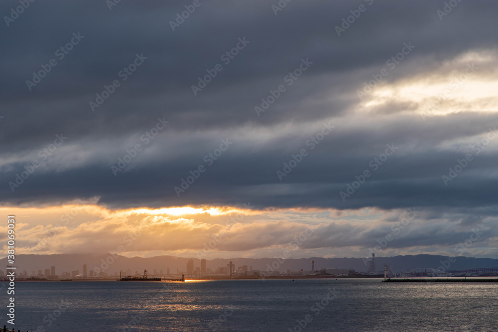 兵庫県神戸市から大阪湾の夜明け。厚い雲に覆われた空に太陽の光が現れる