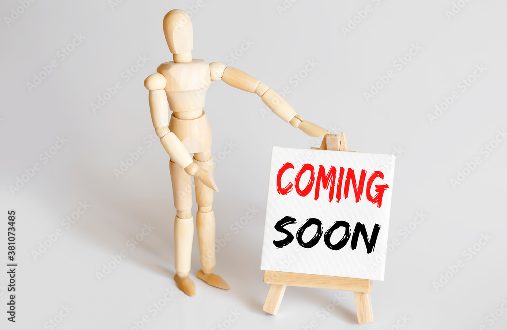 Wooden man shows with a hand to white easel with text COMING SOON Wooden man shows with a hand to white easel with text COMING SOON