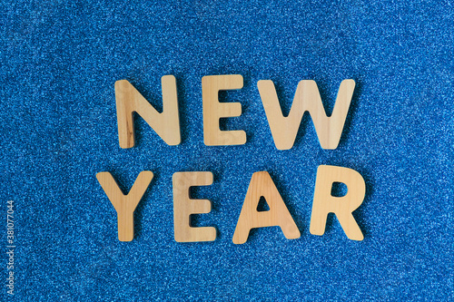 Wooden inscription New Year on a blue glittering background. New Year's wish, holiday decoration