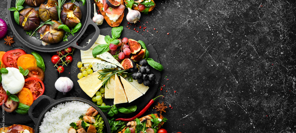 Food: cheese, figs, mushrooms, meat and vegetables. European and Asian cuisine. Healthy food on a black stone background. Top view.