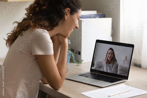 Smiling young woman look at laptop screen talk on video call with girlfriend at home. Happy millennial Caucasian female have pleasant webcam digital virtual conference or conversation on computer.
