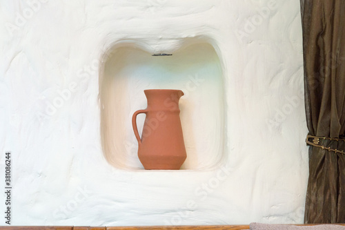 Fototapeta A brown jug in a niche on a white wall.