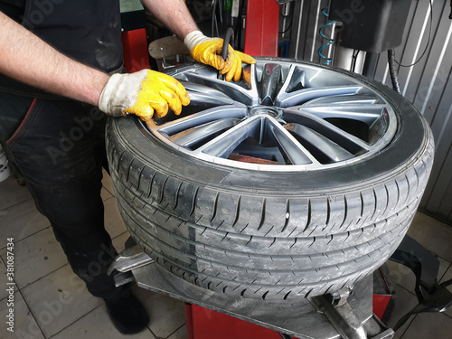 Tire service.. The hands of the car mechanic holding a wheel with the tire. Mechanic inflates the wheel through the nipple
