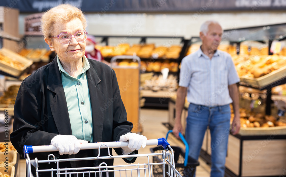 older european woman with glasses shopping in bread section of supermarket