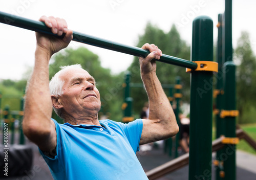 mature cheerful pensioner man doing physical exercises on sports equipped playground