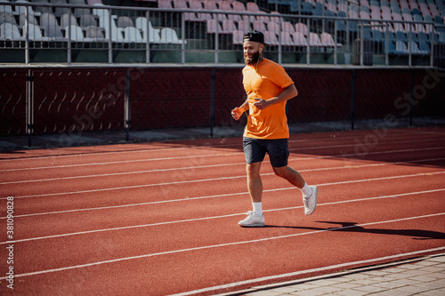 Healthy lifestyle. Handsome male athlete with long beard running while listening to music using earphones.