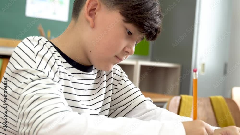 Caucasian school boy in school writing in book with pencil, studying, education, learning. Male student sitting at desk in classroom with notebook in exam Caucasian school boy in school writing in book with pencil, studying, education, learning. Male student sitting at desk in classroom with notebook in exam