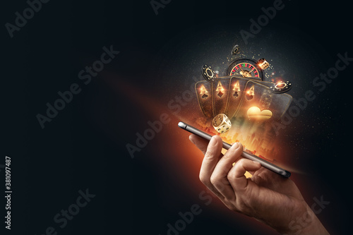 Foto Creative background, online casino, in a man's hand a smartphone with playing cards, roulette and chips, black-gold background