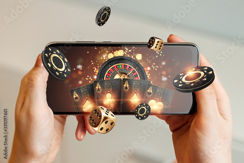 Creative background, online casino, in a man's hand a smartphone with playing cards, roulette and chips, black-gold background. Internet gambling concept. Copy space photo