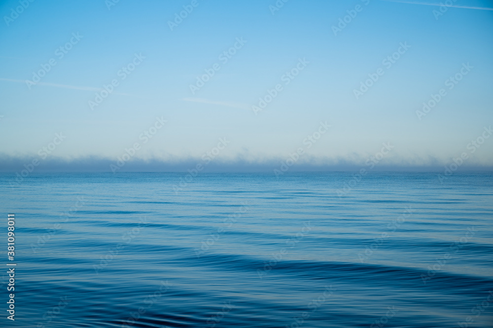 ocean with light waves in bright blue as a conceptual background with a horizon shrouded in light fog and plenty of space for text or design