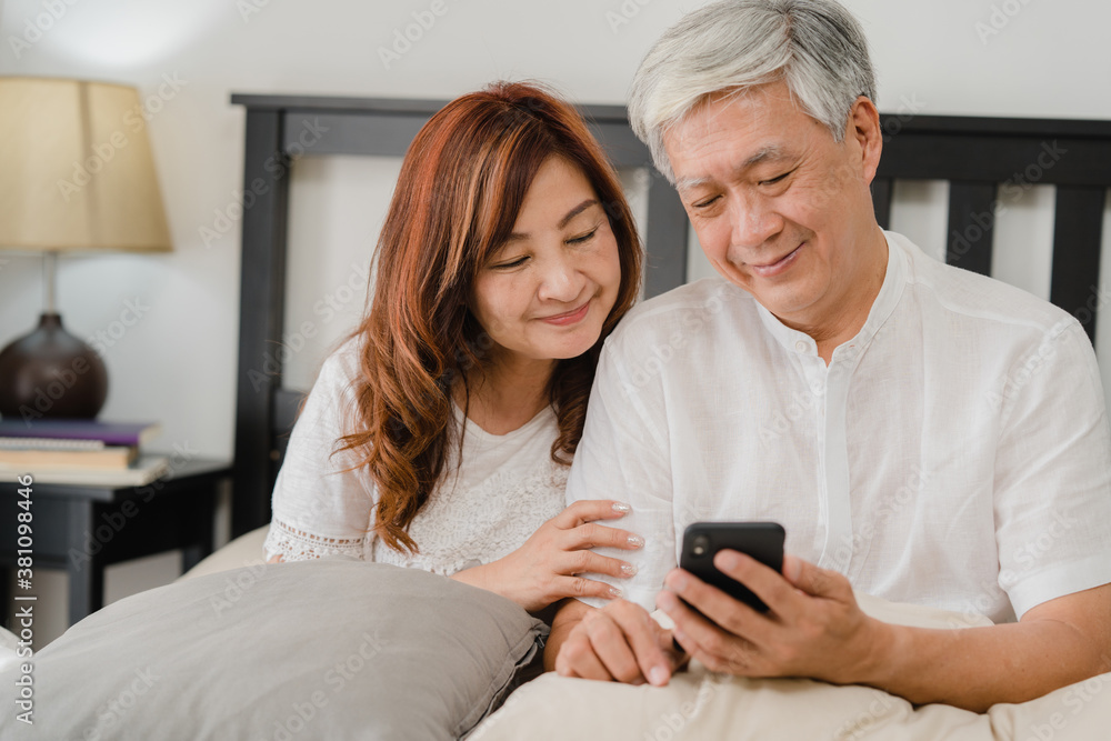 Asian senior couple using mobile phone at home. Asian Senior Chinese grandparents, husband and wife happy after wake up, watching movie lying on bed in bedroom at home in the morning concept. Asian senior couple using mobile phone at home. Asian Senior Chinese grandparents, husband and wife happy after wake up, watching movie lying on bed in bedroom at home in the morning concept.