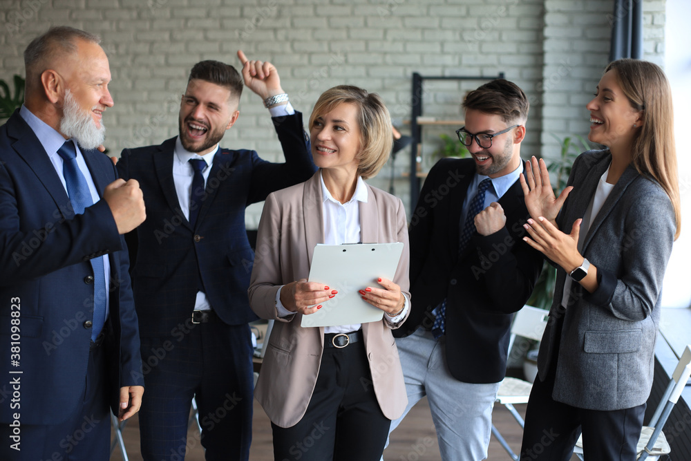 Happy modern business people are keeping arms raised and expressing joyful while standing in office.