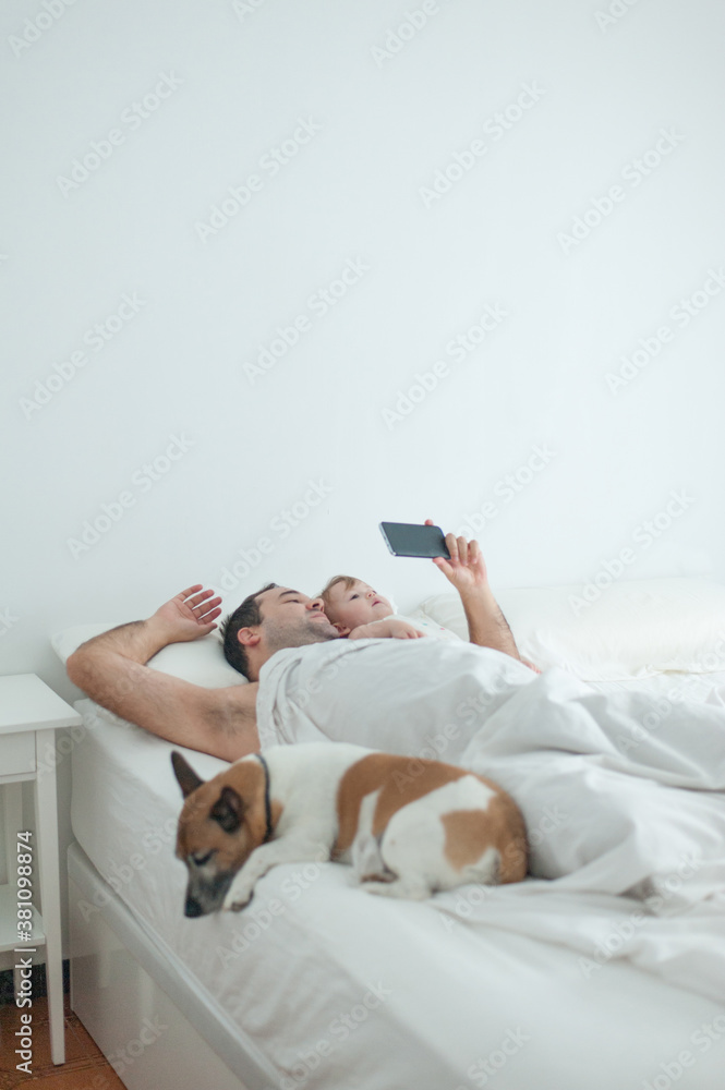 Dad and baby looking smartphone in bed with dog Dad and baby looking smartphone in bed with dog
